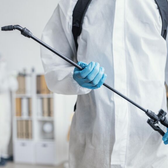 Technicien en traitement antiparasitaire à domicile portant un équipement de protection et préparant un pulvérisateur, avant une intervention nécessitant de quitter temporairement la maison.